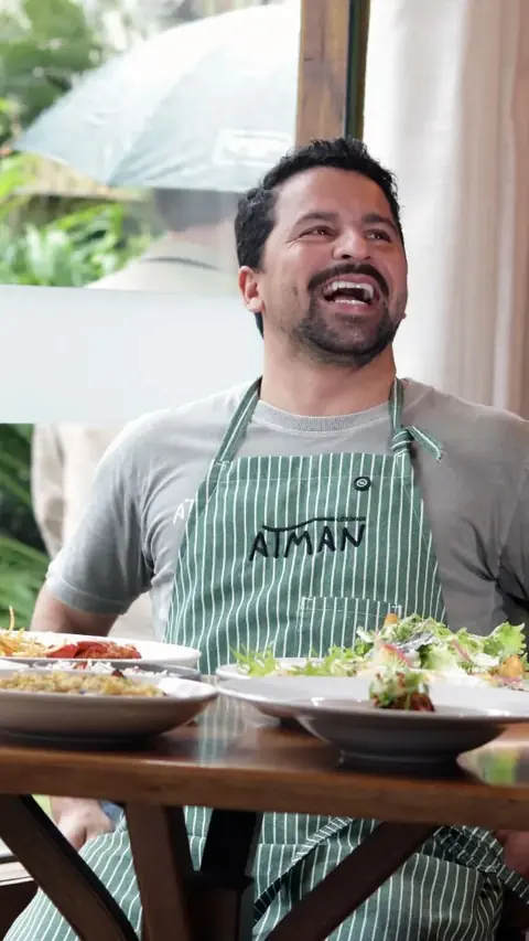 Chef Alan Marcos gargalhando, de avental listrado, com pratos à frente
