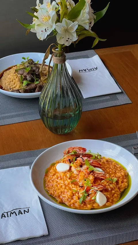 Mesa de madeira com dois pratos, vaso de flores brancas e guardanapos do Atman