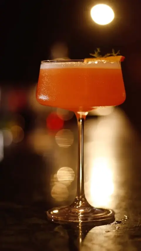 Coquetel laranja em taça, com luzes da noite ao fundo